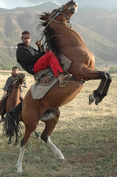 a man riding on the back of a brown horse next to another person in a field