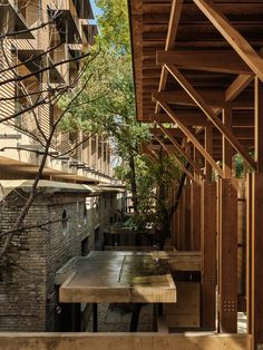 an outdoor dining area with wooden benches and tables on the side of the building, surrounded by trees