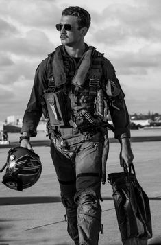 a man walking down an airport tarmac with his helmet and goggles in hand