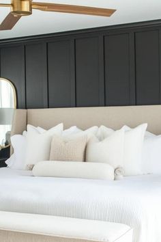 a bed with white sheets and pillows next to a large mirror on the wall above it