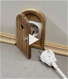 an electric outlet plugged in to a wooden door shaped like a toilet paper dispenser