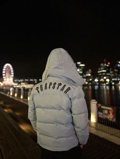 a person in a white jacket looking out at the water and ferris wheel behind them