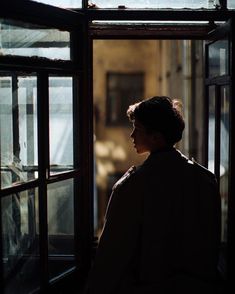 a woman standing in front of a window looking out at the street below her is an old building