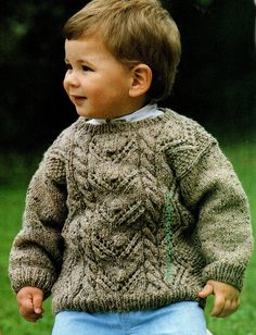 a little boy standing in the grass wearing a sweater