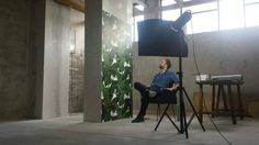 a man sitting in a chair next to a camera on a tripod and another person standing up behind him