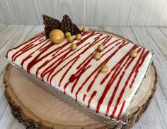 a piece of cake with white and red icing on a wooden slice that is sitting on a table