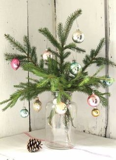 a glass vase filled with christmas ornaments on top of a white tablecloth next to a pine cone