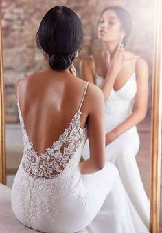 a woman sitting in front of a mirror looking at her reflection wearing a wedding dress