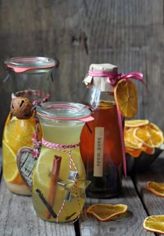 three jars filled with different types of liquid next to sliced oranges and cinnamon sticks