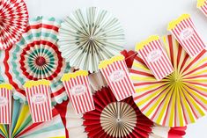 colorful paper fans are lined up against a white wall with red and yellow tags on them