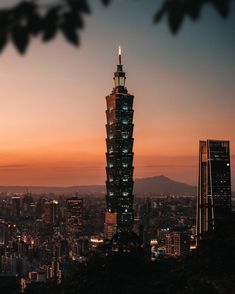 a tall building towering over a city at sunset or dawn with the sun setting in the distance