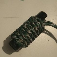 a green and white rope wrapped around a black object on the floor in front of a wall