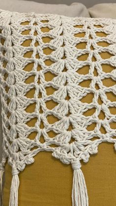 a white crocheted pillow with tassels on the sides and a yellow cushion behind it