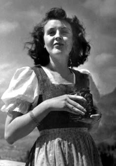 an old black and white photo of a woman holding a camera in her hands with mountains in the background