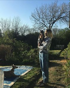 a woman holding a dog in her arms while standing next to an animal on a blanket