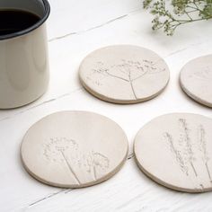 four white ceramic coasters sitting on top of a table next to a coffee cup