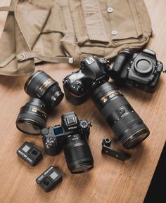 several cameras sitting on top of a wooden table next to a bag and some other items