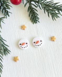 two crocheted snowmen are sitting next to pine branches and ornaments on a white surface