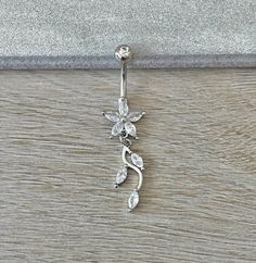 a close up of a flower belly button ring on a wooden surface with a silver background