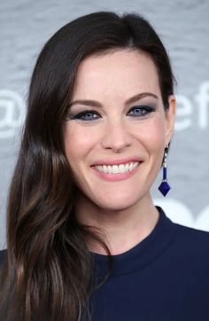 a woman with long hair and blue eyeshadow smiles at the camera while wearing earrings