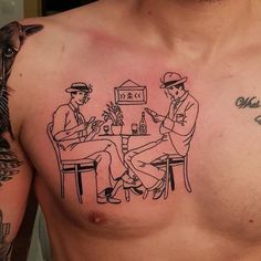 a man with tattoos on his chest is sitting at a table while two other men are eating