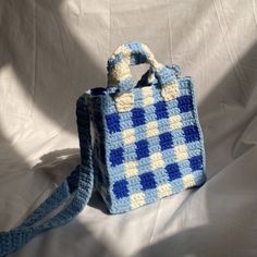 a crocheted blue and white bag sitting on top of a white cloth covered bed