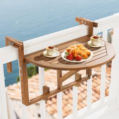 two plates of food sit on a wooden table overlooking the water and buildings in the distance