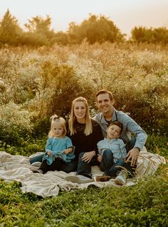 a family sitting on a blanket in the middle of a field with tall grass and bushes