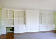 an empty room with white bookcases and hardwood floors in front of green walls