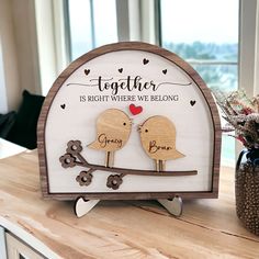 a couple of birds sitting on top of a wooden sign next to a vase filled with flowers