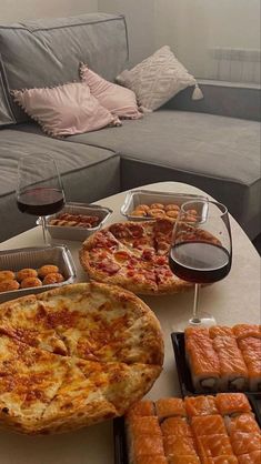 a table with pizzas and drinks on it in front of a couch that is filled with pastries