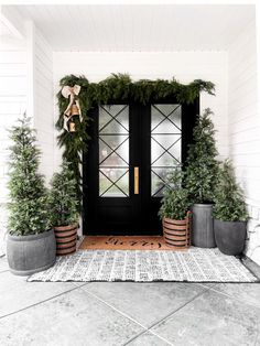 the front door is decorated for christmas with potted trees and wreaths on it