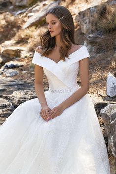 a woman in a white wedding dress sitting on some rocks and looking off to the side