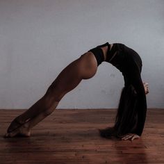 a woman in black shirt doing a handstand on wooden floor next to wall