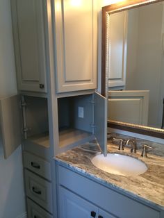 a bathroom vanity with marble counter top and white cabinetry, mirror above the sink