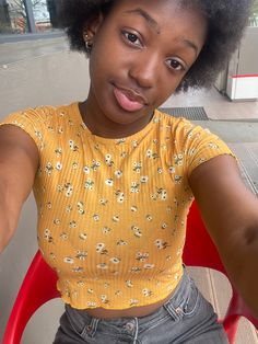 a woman sitting in a red chair with an afro on her head and wearing a yellow shirt