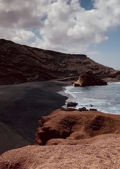 there is a large body of water on the beach near some rocks and sand with mountains in the background