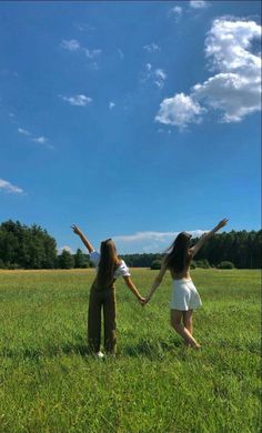 two girls are standing in the middle of a field holding their hands up to the sky