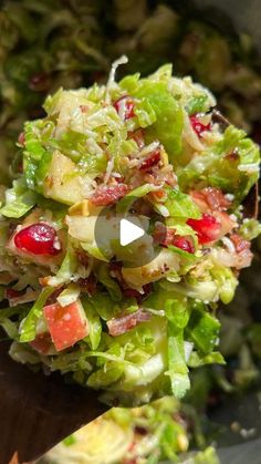 a salad with apples and cranberries is being held up by a wooden spoon