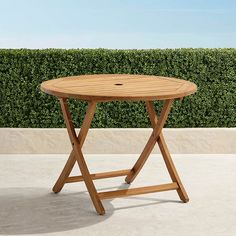 a wooden table sitting on top of a cement floor next to a green hedge covered wall