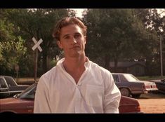 a man is standing in front of some parked cars and looking at the camera while wearing a white shirt