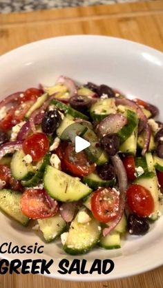 a white bowl filled with cucumber, tomatoes and olives on top of a wooden table