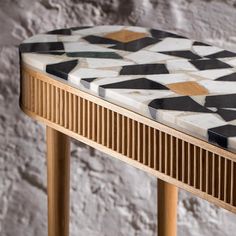 a wooden table with black and white tiles on it's top, next to a brick wall