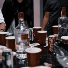 a group of people standing around a table filled with bottles and cups on top of it