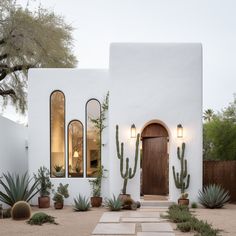 a white stucco house with cactus and succulents in the front yard at dusk