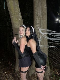 two women dressed up in costumes standing next to each other by a tree at night