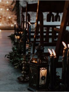 many lit candles are lined up on the floor in front of chairs with greenery