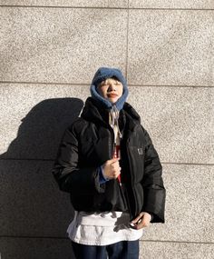 a person standing in front of a wall wearing a coat and holding an umbrella with both hands