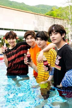 group of young men standing next to each other in a pool holding drinks and posing for the camera