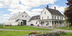 two large white houses sitting next to each other on a lush green field with clouds in the sky